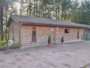 A log cabin with a front porch, two potted evergreen trees, and a gravel driveway.