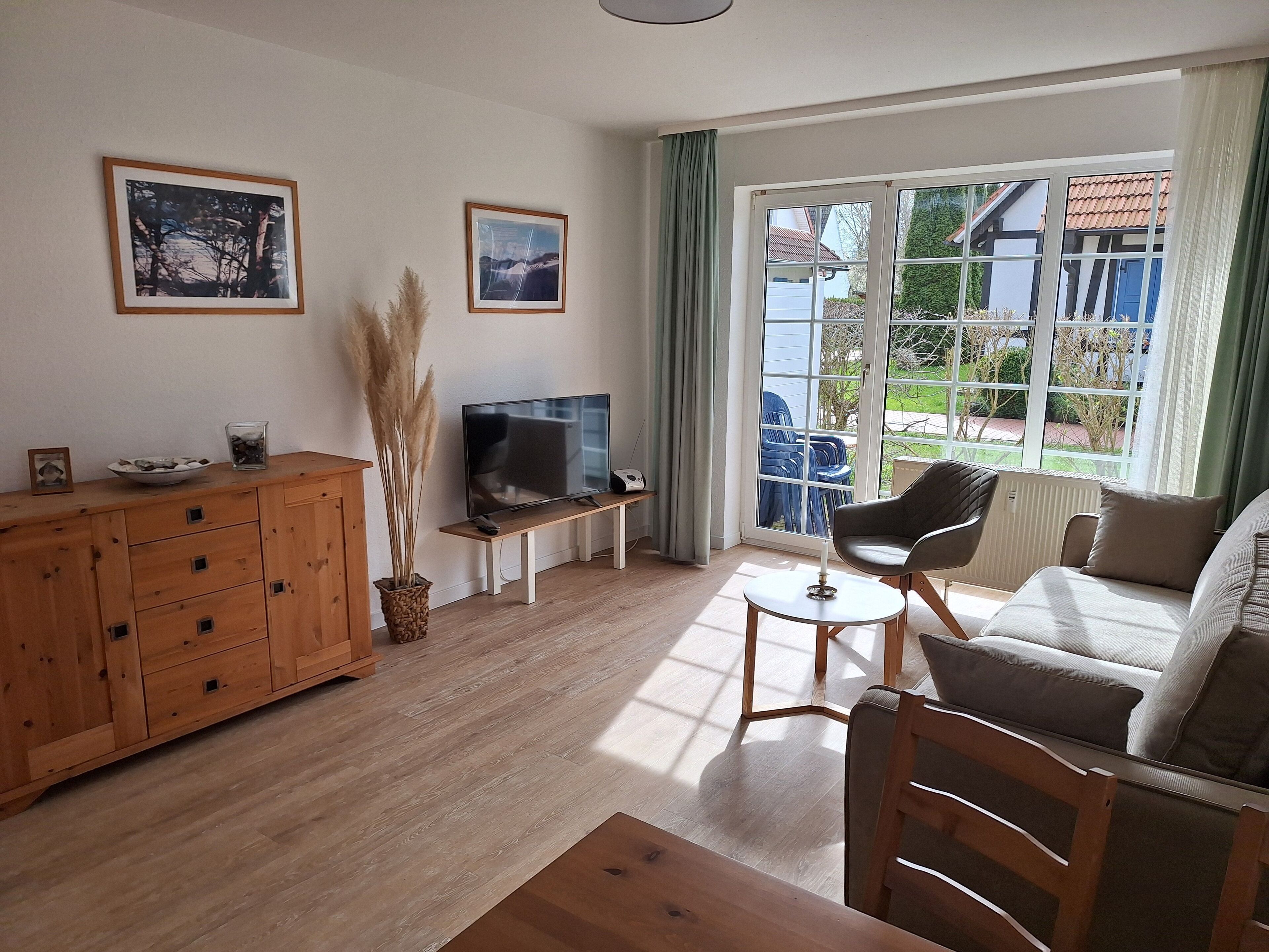 A living room with a wooden cabinet, a TV on a stand, a sofa, and a window with a view of the outside.
