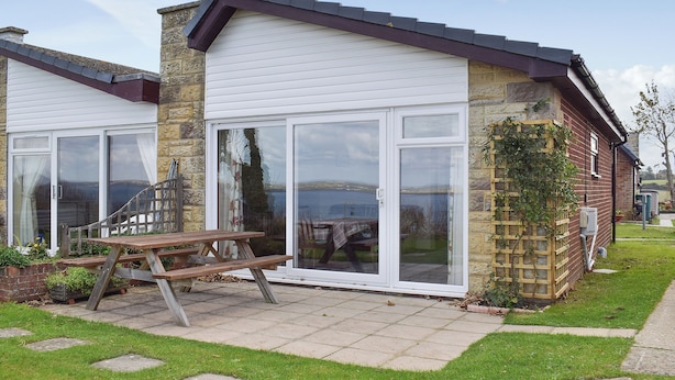 A house with a patio, a wooden table, and a stone wall. - 2 bedroom accommodation in Freshwater (Freshwater)