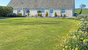 Une maison en pierre avec un toit en pente, une cheminée et une pelouse bien entretenue.