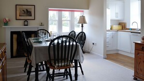 Een eetkamer met een tafel voor vier personen, een open haard en uitzicht op de keuken.