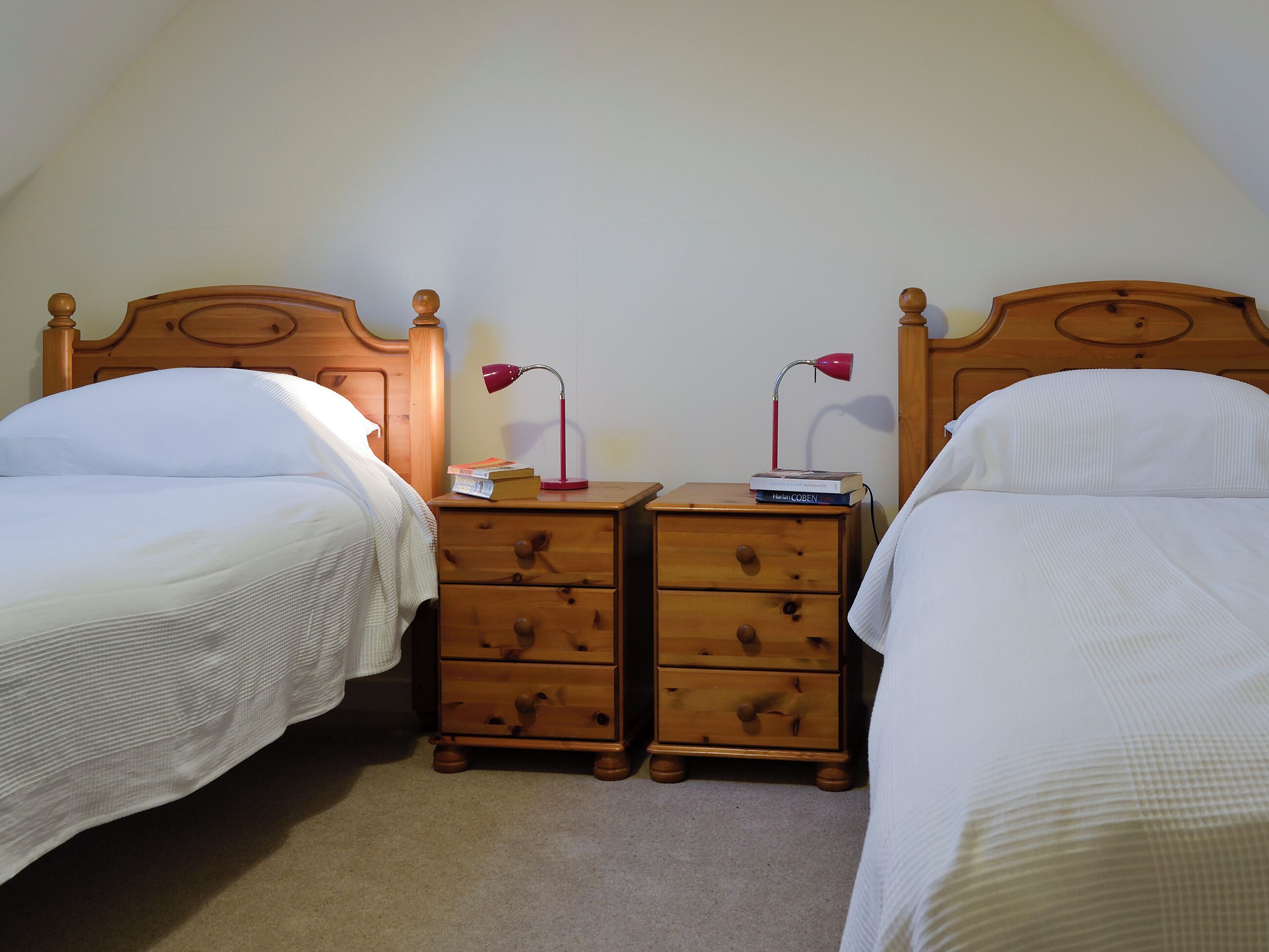 Une chambre avec deux lits simples, des tables de chevet en bois dotées de tiroirs et une lampe de bureau rouge.