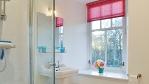 Een badkamer met een douchecabine van glas, een wastafel met spiegel, een raam met uitzicht op bomen en een toilet.