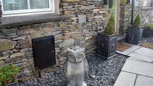 A stone building with a window, a stone wall, and a small garden with plants and a stone statue. - 3 bedroom accommodation in Ambleside (Ambleside)