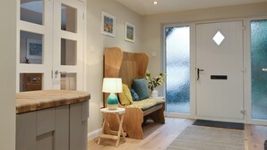 A modern interior with a wooden bench, a small table with a lamp, and a frosted glass door. - 4 bedroom accommodation in Lansallos, near Looe (Lansallos, near Looe)