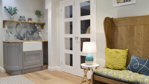 A modern kitchen with grey cabinets, a wooden countertop, and a sink. There is a white door with glass panels and a small table with a lamp. A wooden bench with cushions is against the wall. - 4 bedroom accommodation in Lansallos, near Looe (Lansallos, near Looe)