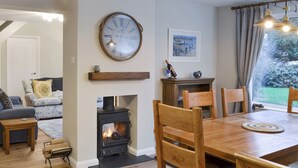 A cozy living room with a fireplace, wooden furniture, and a clock on the wall. - 4 bedroom accommodation in Lansallos, near Looe (Lansallos, near Looe)