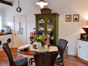 A dining area with a round table, wicker chairs, a green cabinet with glass doors, and a clock on the wall.