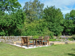 An outdoor seating area with a stone wall, wooden furniture, and a garden backdrop.