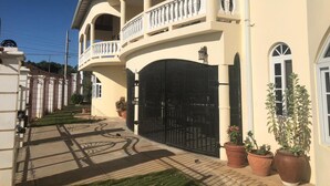 A two-story house with a balcony, a gated entrance, and potted plants. - Retreat Comfortable Apartments (Falmouth)