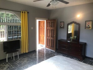 A bedroom with a bed, a dresser, a mirror, and a window with curtains.