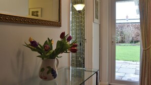 Een kamer met een glazen tafel, een vaas bloemen, een spiegel en een deur die naar buiten leidt.