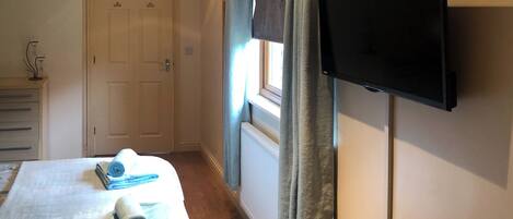 Ein Schlafzimmer mit einem Bett, einem an der Wand befestigten Fernseher, einer Tür und einem Fenster mit Vorhängen.