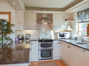 A kitchen with white cabinets, stainless steel appliances, a tiled backsplash, and a window with a view of the outside. - Yorkshire Rose Holiday Lodge (Sewerby, near Bridlington)