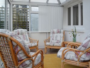 Une véranda meublée de mobilier en osier et agrémentée d’un tapis jaune.