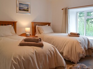 Una habitación de hotel con dos camas, una mesita de noche con lámpara y una ventana con cortinas.
