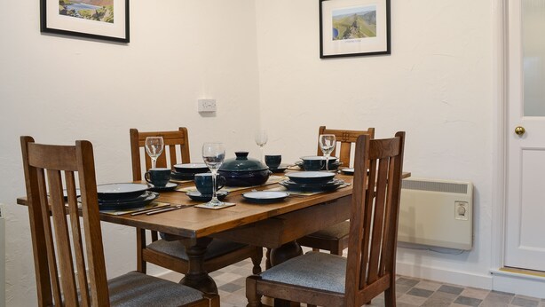 Un comedor con una mesa de madera dispuesta para cuatro personas, rodeada por cuatro sillas de madera con asientos acolchados. Hay cuadros enmarcados en las paredes sobre la mesa.