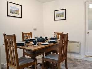 Une salle à manger avec une table en bois dressée pour quatre personnes, entourée de quatre chaises en bois dotées d’assises rembourrées. Des tableaux encadrés ornent les murs au-dessus de la table.