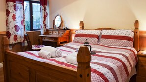 A bedroom with a wooden bed, a wooden dresser, a mirror, and a window with floral curtains.