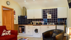 A compact living space with a kitchen, a red sofa, a black leather chair, and a small wooden table.