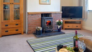 A cozy living room with a brick fireplace, a television, a cabinet with glass doors, and a striped rug. - 2 bedroom accommodation in Mabie, near Dumfries (Mabie, near Dumfries)