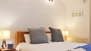 Ein ordentlich bezogenes Bett mit grau-weißen Textilien, zwei Nachttischlampen und ein gerahmtes Bild an der Wand.