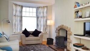 Ein Wohnzimmer mit Kamin, einer Couch, einem Sessel, einer Lampe und einem Bücherregal.