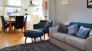 Ein Wohnzimmer mit einer Couch, Sesseln, einem Esstisch und einer Küchenzeile im Hintergrund.