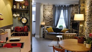 Un espacio habitable compacto con kitchenette, comedor y zona de estar con pared de piedra y sofá.