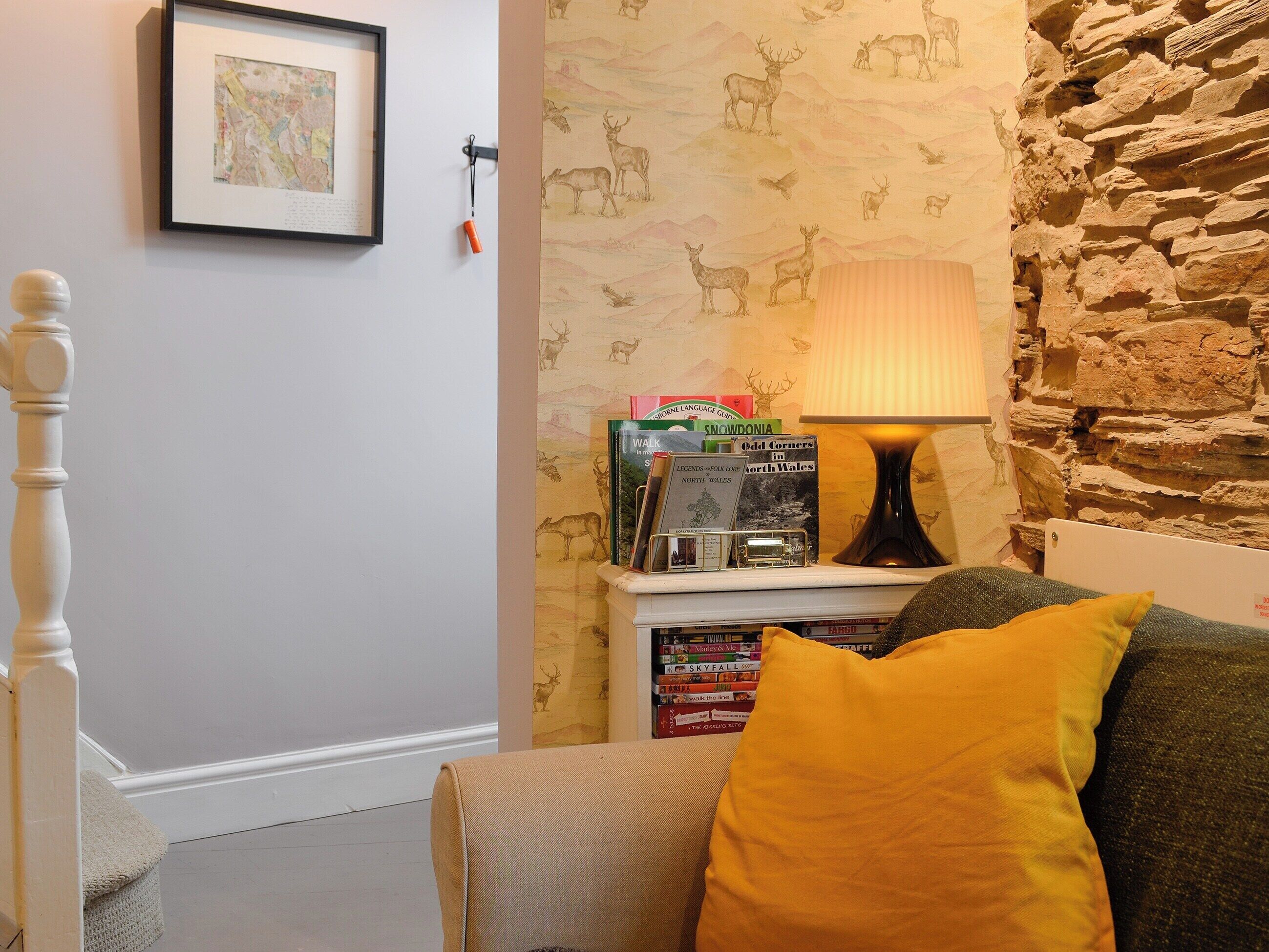 A cozy room with a bookshelf, a lamp, and a stone wall.