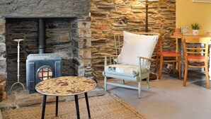 Una habitación acogedora con pared de piedra, chimenea, una mesa redonda y una silla.