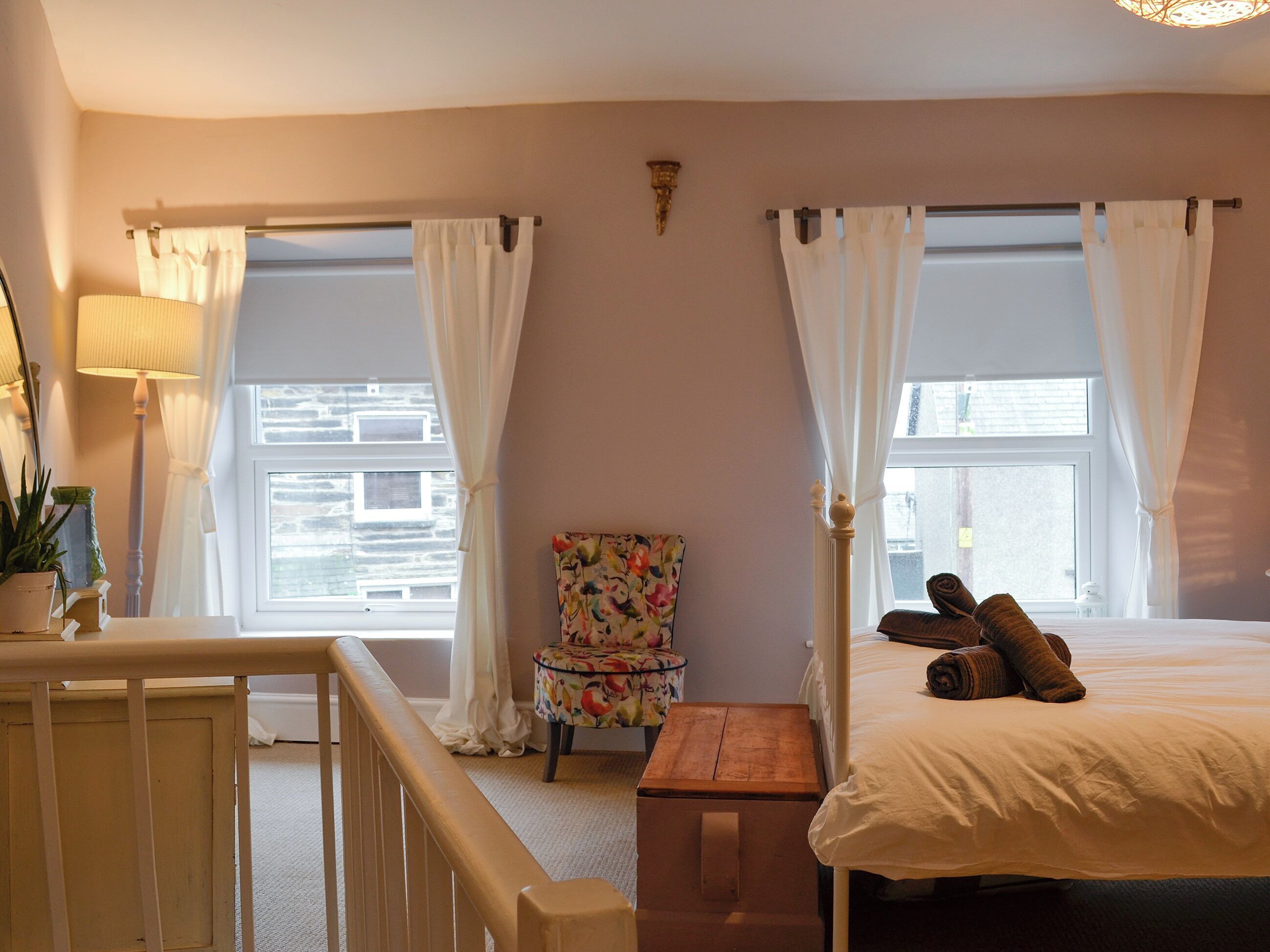 Une chambre à coucher avec un lit, une table de chevet, une chaise et une fenêtre avec des rideaux.