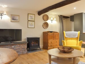 A living room with a TV, a fireplace, wooden furniture, and wall decorations. - 1 bedroom accommodation in Stickle Path, near Watchet (Stickle Path, near Watchet)