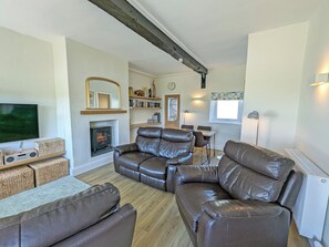 A living room with a fireplace, leather sofas, a TV, and a dining area.