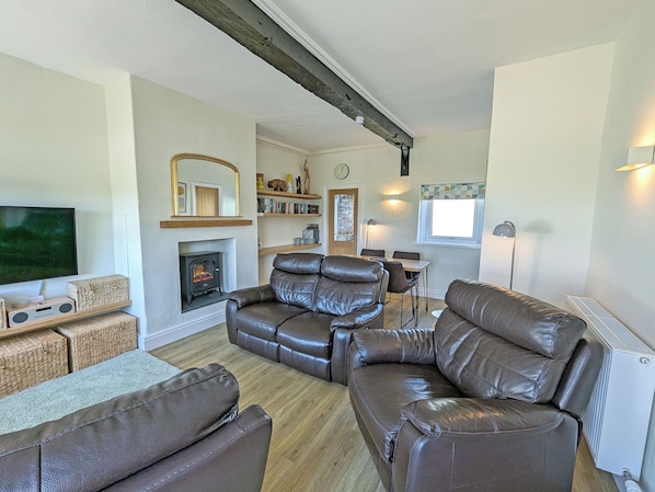 A living room with a fireplace, leather sofas, a TV, and a dining area.