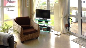 A living room with a brown wicker chair, a glass coffee table with a flat-screen TV, and a sliding glass door leading to an outdoor area.