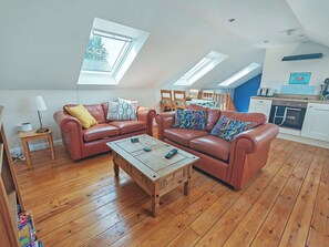 A living room with two leather sofas, a wooden coffee table, and a dining area with a kitchen in the background.