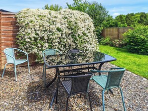 Une terrasse avec une table et des chaises, entourée d’un jardin agrémenté d’un grand arbuste en fleurs.