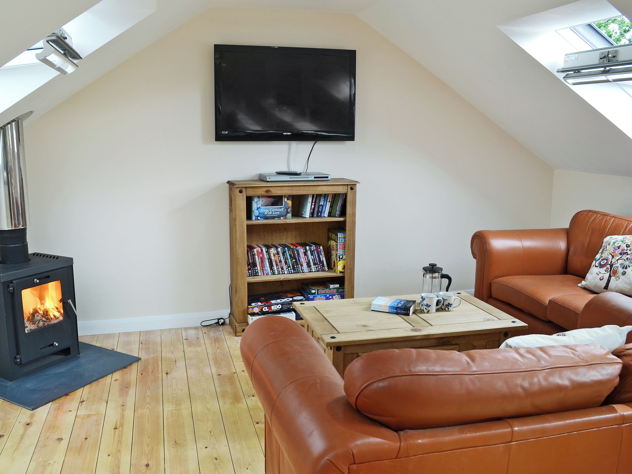 A cozy loft bedroom with a wood-burning stove, a bookshelf, a leather sofa, and a flat-screen TV.