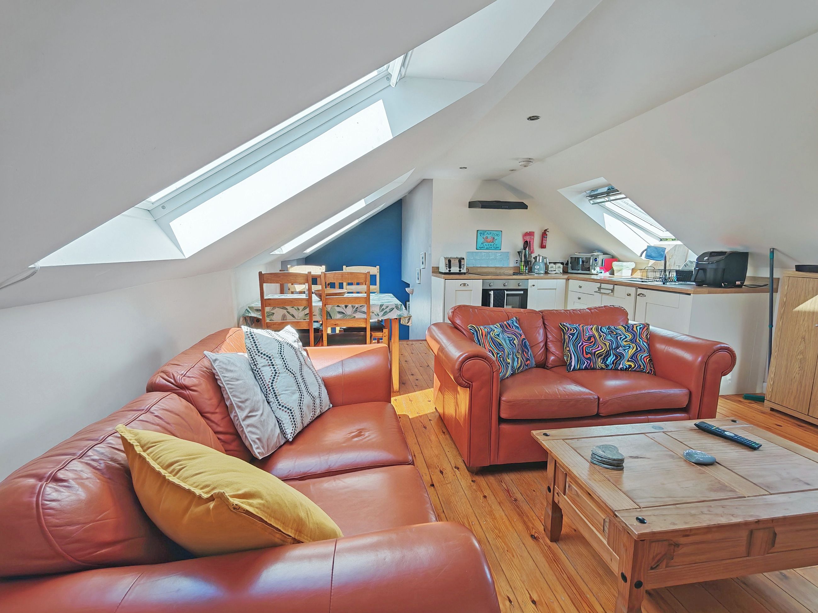 Un espace de vie de style loft avec un plafond haut, un coin repas avec une table et des chaises, un coin cuisine et un canapé en cuir rouge agrémenté de coussins à motifs.