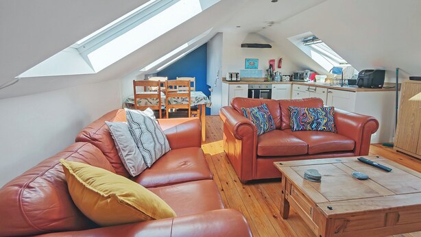 A loft-style living space with a high ceiling, a dining area with a table and chairs, a kitchenette, and a red leather sofa with patterned cushions. - 2 bedroom accommodation in Derril, near Bude (Derril, near Bude)