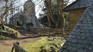 Ein historisches Steinhaus mit einem markanten Turm, umgeben von Bäumen und einem Holzzaun.