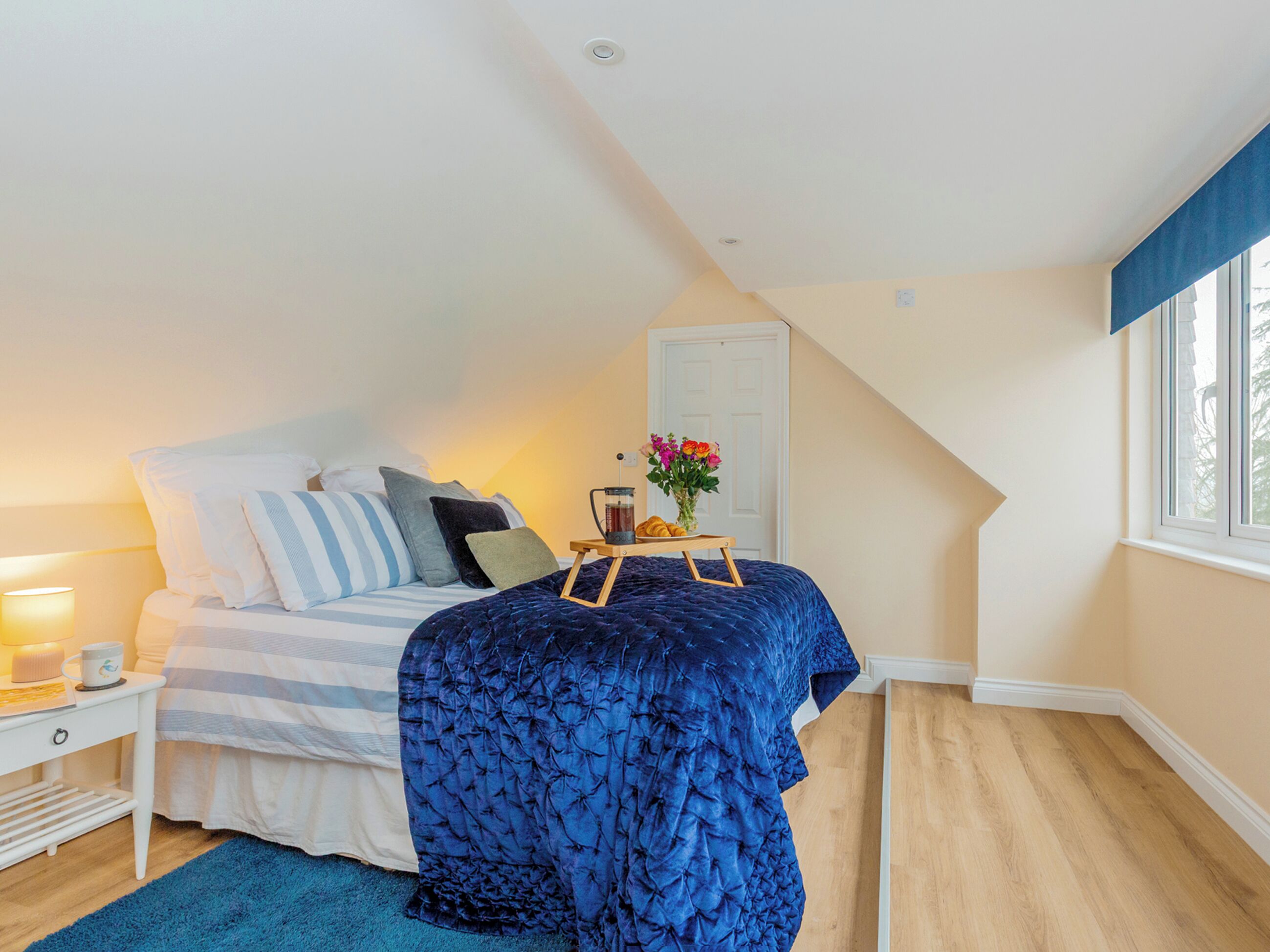 Ein Schlafzimmer mit Bett, Nachttisch, Lampe und einem Fenster mit Vorhängen.