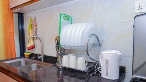 Una cocina con un escurreplatos lleno de platos y tazas, una cafetera y un lavabo con grifo.