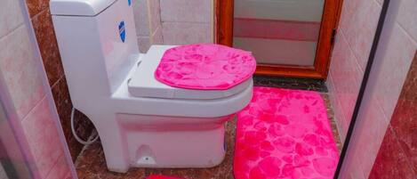 A small bathroom with a toilet, a pink mat on the floor, and a shower area.
