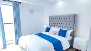 Un dormitorio moderno con una cama grande, un cabecero capitonado, una alfombra mullida y una mesita de noche.