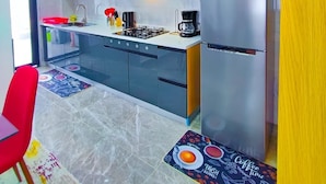 Una cocina moderna con armarios blancos, un refrigerador de acero inoxidable, una estufa a gas y una cafetera.
