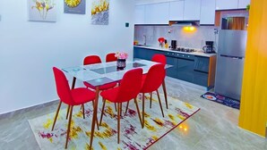 Un comedor moderno con una mesa de vidrio y sillas rojas, una cocina con electrodomésticos de acero inoxidable y obras de arte en las paredes.