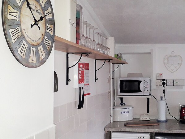 A kitchen with a vintage clock, a microwave, and a bread maker.