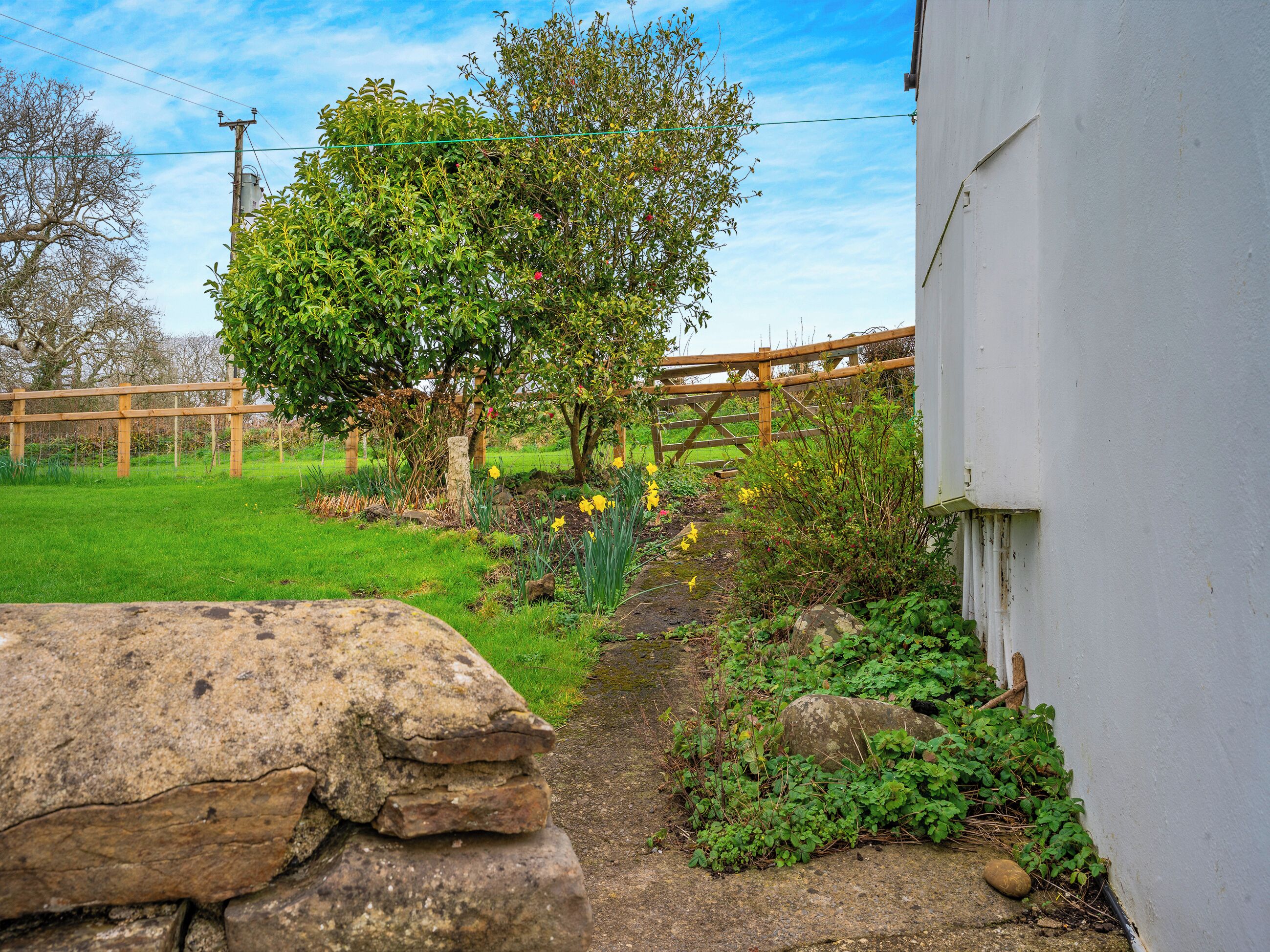 A garden with a wooden fence, a stone wall, and a white building.
